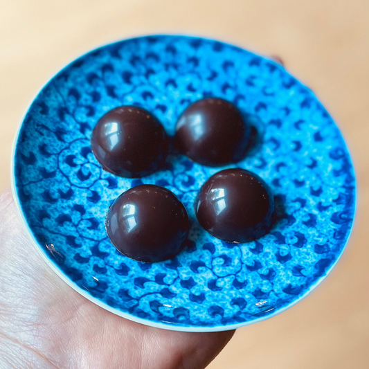 Unwrapped salted caramel bonbons with glossy finish on small blue plate, held in palm of hand